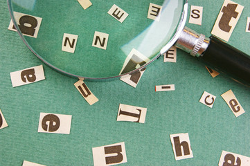 Fototapeta na wymiar letters cut from newspaper and magnifying glass on green background