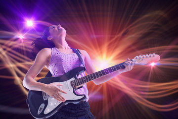 Pretty girl playing guitar against curved laser light design in orange
