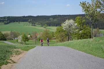 Obraz premium Spring bike riding on the beautiful hills, Young couple on bikes riding on the beautiful green hills during beautiful spring day