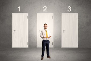 Fototapeta premium Businessman in grey room with three numbered white door behind his back 
