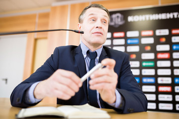 Low angle portrait of mature businessman speaking to microphone at press conference