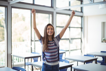 Excited schoolgirl standing with arms up in classroom