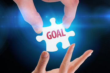 The word goal  and hands holding jigsaw against blue background with vignette