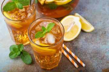 Traditional iced tea with lemon, mint and ice in tall glasses. Two glasses with cool summer drink on old rusty background