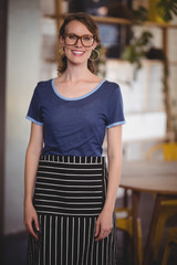 Portrait of smiling young waitress wearing eyeglasses at coffee shop
