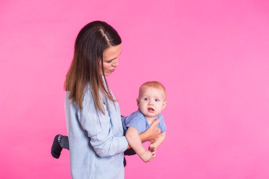 family, motherhood, parenting, people and child care concept - happy mother holds adorable baby over pink background