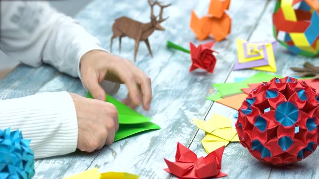 Man at origami folding lesson. Collection of beautiful origami figurines on wooden table. Traditional origami paper folding.