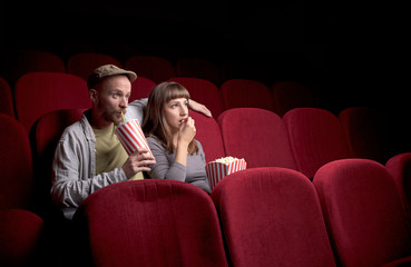 Young cute couple sitting alone at red movie theatre and having fun