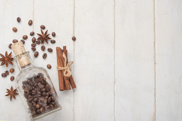 Grains of coffee in a glass jar, with cinnamon and badan, on a light wooden texture. With empty space for writing