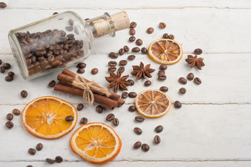 Grains of coffee in a glass jar, with cinnamon and buckwheat, dried oranges, on a light wooden texture.
