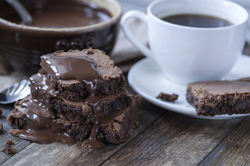 Homemade chocolate brownies with coffee on wooden background, chocolate souce on ceramic bowl