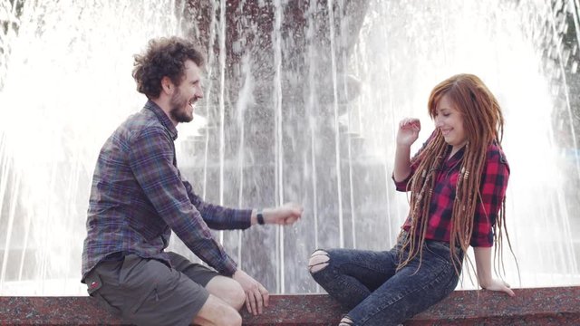 Young couple posing near fountain in sunny summer day, male and female tourists having good time, couple of hipsters on vacation