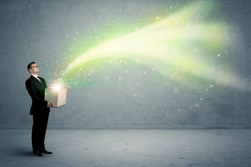 Bright yellow, green light beams escaping a cardboard box held by young elegant male business person in stylish suit concept.