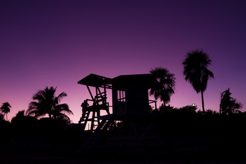 Silhouette of baywatch tower and palm trees at sunset in Playa del Carmen, Mexico. Lifeguard wooden...