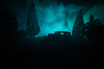 Silhouette of old vintage car in dark foggy toned background with glowing lights in low light, or silhouette of old car in dark forest.