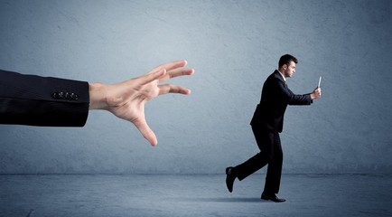 Young miniature businessman running from a big hand with blue background