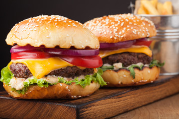 Close-up of delicious fresh home made burger with lettuce, cheese, onion and tomato on a dark background. fast food and junk food concept