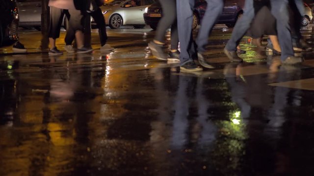 PARIS, FRANCE - SEPTEMBER 29, 2017: Pedestrians crossing the wet road on zebra and then cars driving. View at rainy night in autumn