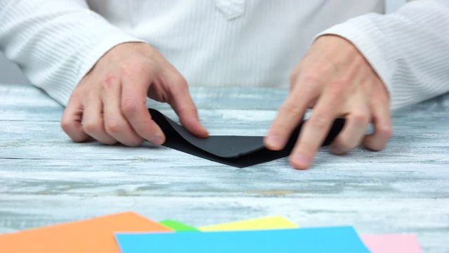 Hands folding black paper sheet. Man making origami close up. How to fold origami swan instructions.