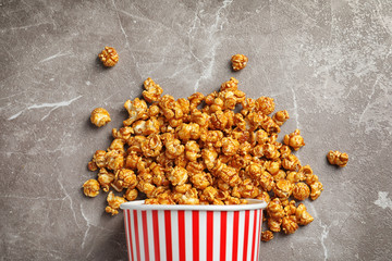 Delicious popcorn with caramel in paper bucket on gray background, top view