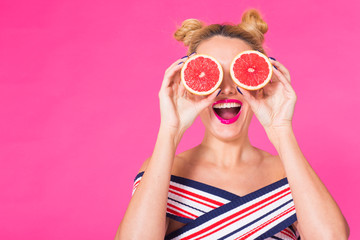 Smiling girl with grapefruit cut in half fruit in hand on pink background with copyspace