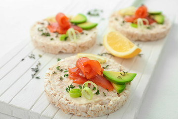 Crispbreads with fresh sliced salmon fillet and avocado on wooden board, closeup