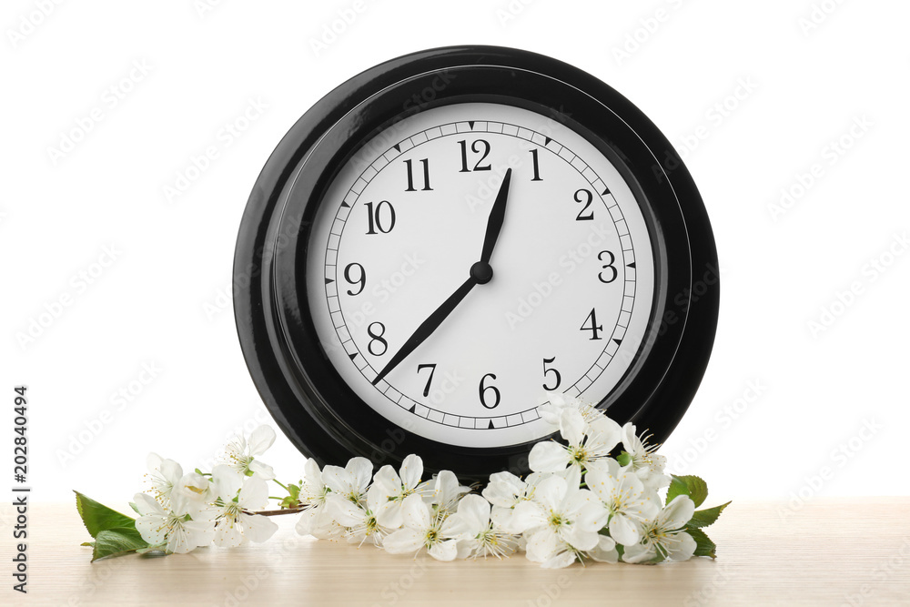 Aufkleber big clock and branch with spring blossoms on table against white background. time change concept