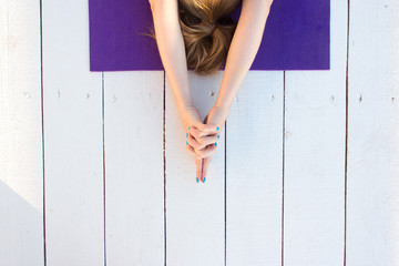 Woman practicing outdoors on violet yoga mat. Overhead close up of female hands in mudra on white wooden background.