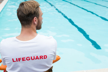 Lifeguard sitting on chair with rescue buoy at poolside