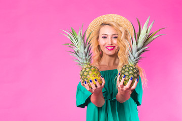 Happy young woman holding a pineapple on a pink background with copyspace. Summer, diet and holidays concept