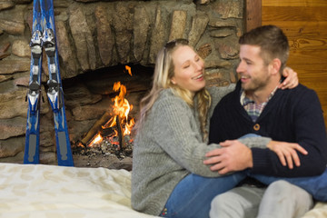 Cheerful couple with arms around in front of lit fireplace