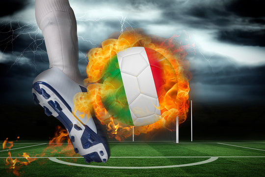 Football player kicking flaming italy flag ball against football pitch under stormy sky