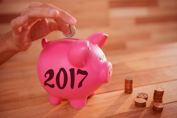 Digital image of new year 2017 against cropped image of hand inserting coin in piggy bank