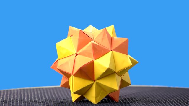 Yellow origami ball on blue background. Kusudama figure on colorful background. Art of folding paper.