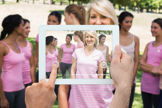 Composite image of hand holding tablet pc showing photograph of breast cancer activists