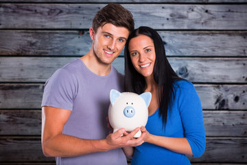 Young couple holding a piggy bank against grey wooden planks