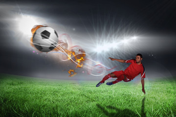 Obraz na płótnie Canvas Football player in red kicking against football pitch under bright lights