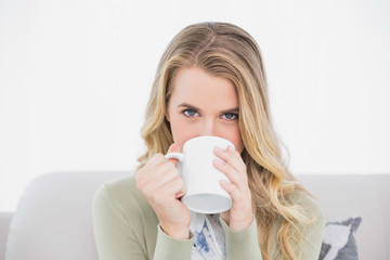 Cute blonde drinking coffee sitting on cosy sofa