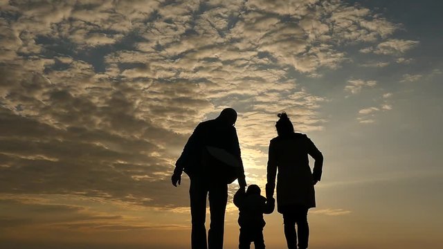 father mother and 1 year old son silhouette walking on sky background slow motion