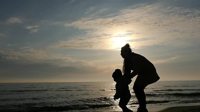Silhouette of walking mother with 1 year son near sea panoramic shot slow motion