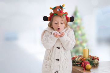 Cute girl blowing over hands against blurry christmas tree in room
