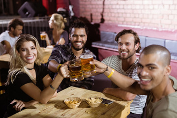 Portrait of happy friends toasting beer mugs at nightclub