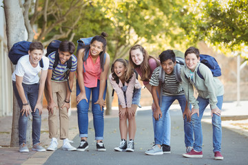 Portrait of happy students standing with schoolbag on road