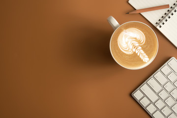 Flat lay, top view office table desk. Workspace with blank note book, keyboard, office supplies  and coffee cup on brown background.