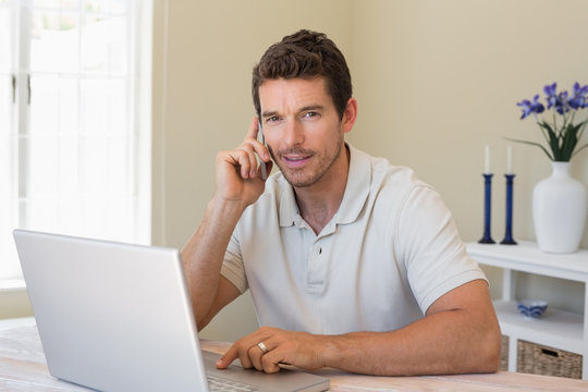 Smiling man using laptop and mobile phone at home
