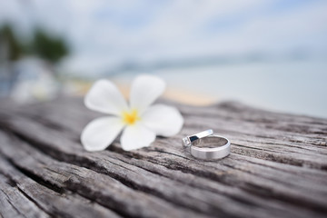 Obraz na płótnie Canvas Wedding rings with wooden table on the beach background