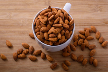 A cup filled with raw almonds on a wooden background