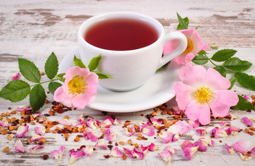 Cup of tea with wild rose flower on rustic wooden background