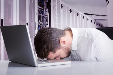 Exhausted businessman sleeping head on laptop against data center