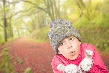 Wrapped up little girl blowing over hands against peaceful autumn scene in forest